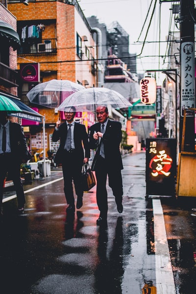 两个身着黑色西装拿着透明的雨伞走在大街上
